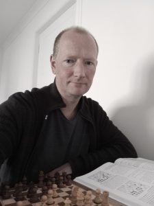 Photo of chess coach Cameron Smith with a chess set and chess book